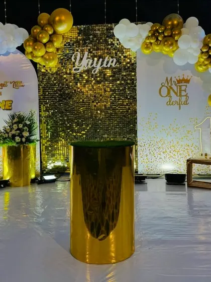 A glamorous first birthday party with a stunning gold sequin wall. The setup is framed by white and gold balloon arches and includes personalized backdrops like "Our Brightest Star is ONE" to make the day extra special.