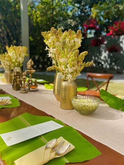 A closer look at the tablescape, featuring brass vases with tuberoses, elegant cutlery, and a custom menu on each banana leaf.
