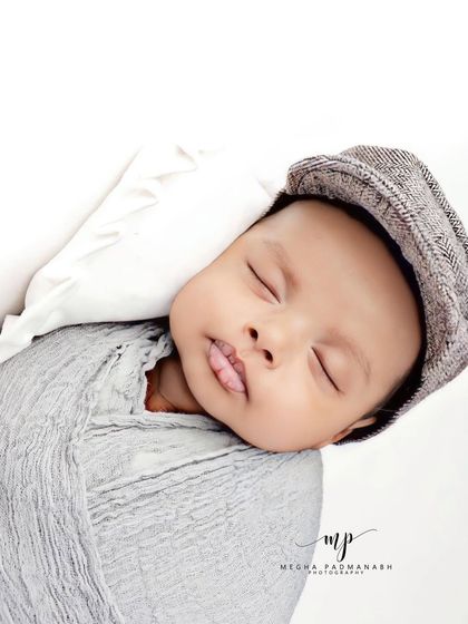 A baby boy in a grey wrap and a dapper newsboy cap, sleeping peacefully.