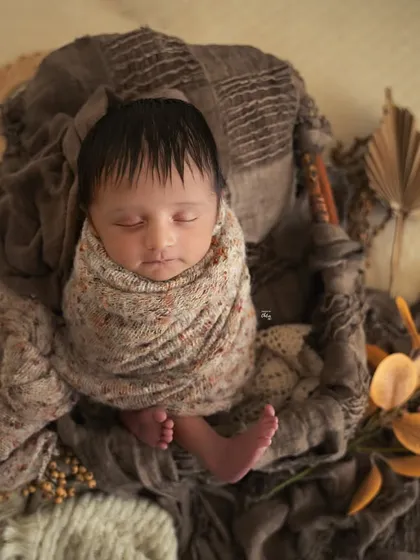A top-down view of a baby in an earthy, neutral-toned setup. The dried leaves and textured wraps create a warm and organic feel.