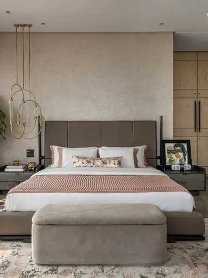 This primary bedroom showcases a thoughtful integration of natural materials like stone and warm veneer paneling. A feature hanging light casts a warm glow, enhancing the room's cozy yet luxurious feel, while a large plant adds a touch of nature.