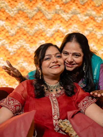 The bride with her mother at the mehendi. Their smiles and embrace capture the love and joy of the celebration, with their outfits reflecting the vibrant and happy mood.
