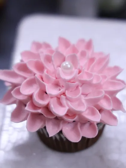 A close-up of a dahlia cupcake made with delicate pink frosting petals and a pearl center. This is one of the techniques I teach in my basic cupcake workshops.