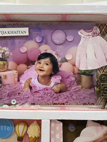 A close-up of the top corner, featuring a photo from a professional baby shoot, complete with a miniature dress and camera embellishment.