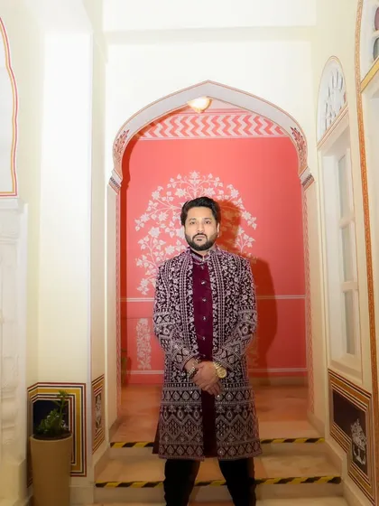 A portrait in a royal maroon sherwani, standing in a beautifully arched hallway. This look is perfect for a grand, traditional Sufi night.