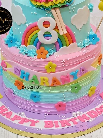 This two-tier butterscotch cake for an 8th birthday features a rainbow color scheme and a cute doll topper. The vibrant layers and floral decorations make it a cheerful and festive centerpiece.