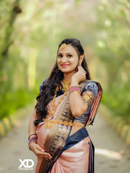 A beautiful close-up portrait of the mother-to-be, showcasing her pregnancy glow and the intricate details of her traditional jewelry and saree.