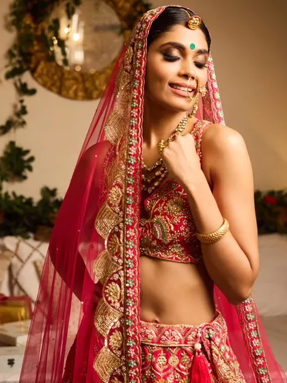 A complete traditional bridal look. The hair is styled in a classic bun adorned with a gajra, and the makeup features a defined eye and a bindi, perfectly complementing the red lehenga and dupatta.