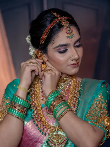 A candid moment of the bride adjusting her earring. This shows the makeup and hairstyle from a different angle, proving its durability.