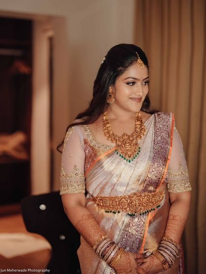 A bride getting ready in her room. The soft lighting creates a serene atmosphere, highlighting the beauty of her pastel saree and custom blouse.