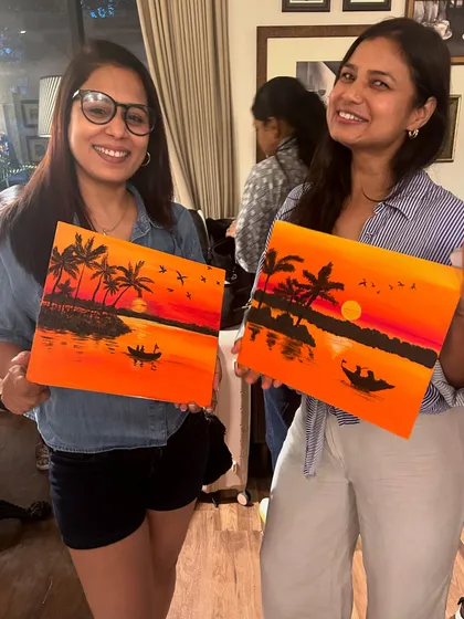 Two participants with their stunning sunset silhouette paintings, featuring palm trees and boats.