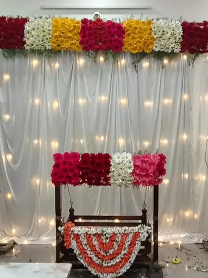 I can transform your living room for an intimate at-home naming ceremony. This decoration includes a beautiful floral arch over a light-up curtain and a cradle decorated with matching fresh flowers.