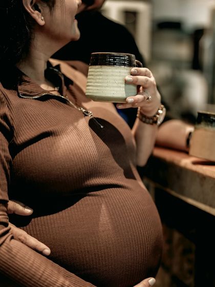 A close-up shot focusing on the baby bump, with the mom-to-be holding a coffee mug. It’s a cozy, lifestyle detail that captures a moment of everyday peace during pregnancy.