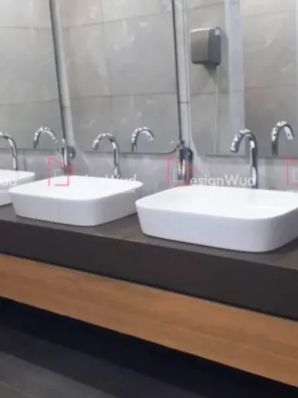 A view of a modern office washroom we designed, focusing on hygiene and durability. The space features multiple vessel sinks on a dark, solid countertop with a wood-laminate base, complemented by large mirrors and easy-to-clean wall tiles. This demonstrates our comprehensive approach to commercial interior projects.