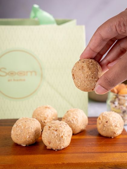 A single, wholesome laddoo held against the backdrop of my signature packaging. This shot emphasizes the simple, handcrafted nature of my sweets.