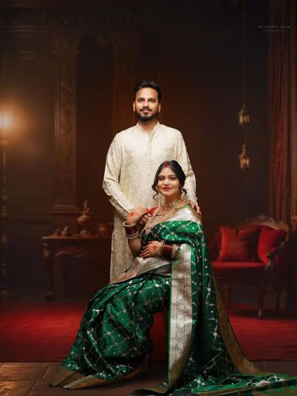 A classic, formal portrait of the couple in traditional attire. This shot showcases the full elegance of the green saree against a rich, dark studio background.