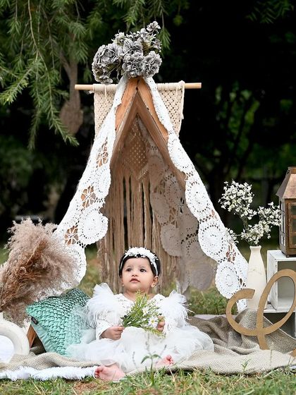 A serene outdoor portrait. This baby girl looks like a little woodland fairy in her lacy white dress, sitting in front of a beautiful handmade teepee.