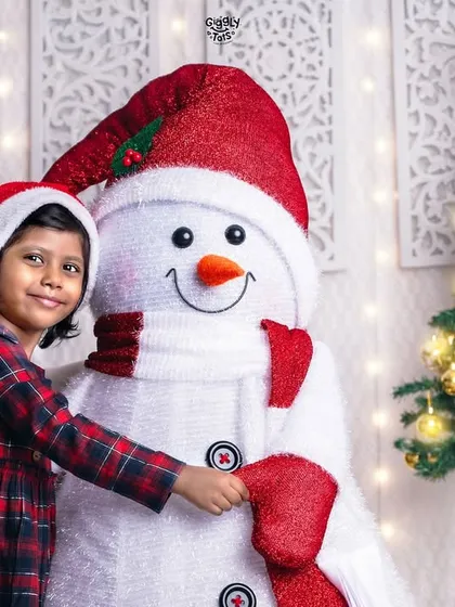 A young girl shares a happy hug with our friendly studio snowman, her smile as bright as the Christmas tree beside them.