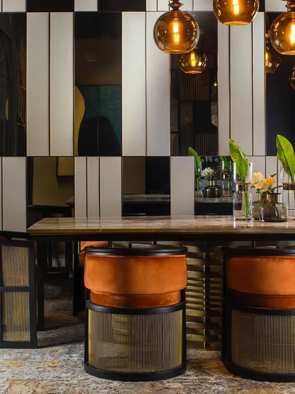 A closer look at our dining chairs, where plush orange velvet upholstery contrasts with a black matt frame and a brass-finished woven metal base. This piece is a study in combining different materials and textures.