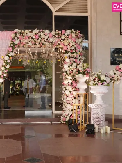 The entrance to this majestic ballroom is framed by a stunning arch of pink and white flowers, setting the stage for a grand and romantic wedding.