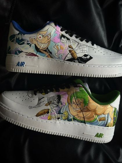 A pair of custom Nike Air Force 1s featuring a detailed illustration of One Piece characters Luffy and Zoro, with contrasting blue and green inner linings.