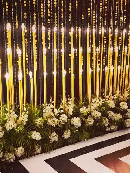A stunning photo backdrop combining hanging beaded curtains and tall candle lamps. The black and white geometric floor adds a bold, modern touch to this glamorous setup.