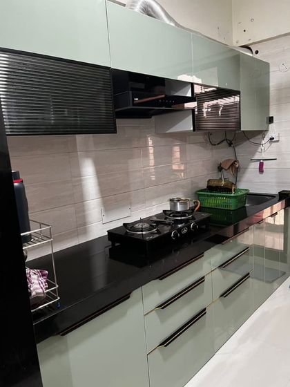 This parallel kitchen in sage green features handleless drawers for a minimalist look. The black countertop and integrated chimney create a seamless and modern design.
