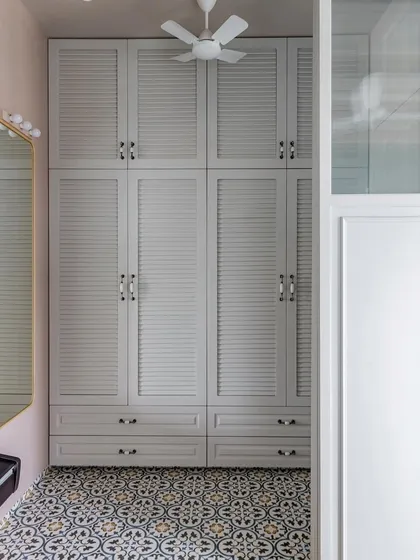 A straight-on view of the elegant walk-in wardrobe. The floor-to-ceiling louvered shutters create a sense of grandeur, while the patterned floor tiles add a touch of playful contrast.