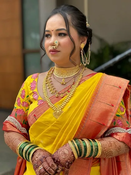 This profile shot highlights the traditional 'kaan vel' ear accessory and the intricate hairstyle, complementing the soft and glowing makeup look.