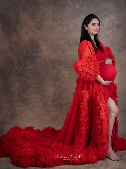 A classic profile shot in a stunning red gown. This pose beautifully highlights the baby bump and the flowing train of the dress for a timeless maternity photo.