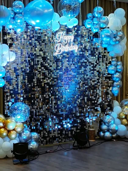 A birthday backdrop with a shimmering blue sequin wall. The "Happy Birthday" neon sign and clusters of blue, white, and gold balloons create a cool, celebratory vibe.