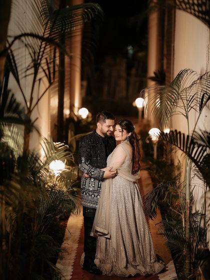 A beautiful portrait in a pathway lit by garden lamps. The warm lighting and lush surroundings create a romantic ambiance for this shot of the couple enjoying a quiet moment together.