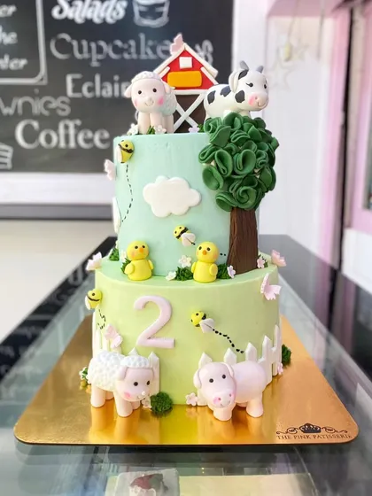 A lovely two-tiered farm animal cake. This design includes a sheep, cow, pig, and chicks, complete with a little red barn and a fondant tree.