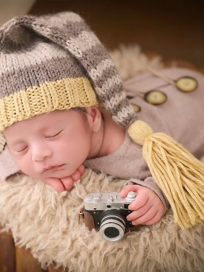 A nod to our own profession, this newborn wears a tassel hat and holds a miniature vintage camera while sleeping on a soft fur rug.