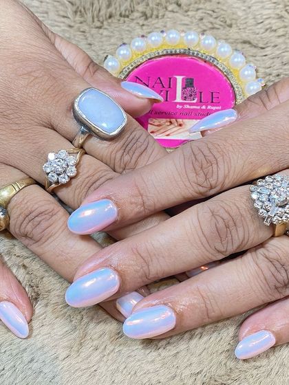 A beautiful iridescent chrome finish. These nails have a pearly, light-blue sheen that catches the light, complemented by the client's stunning rings.
