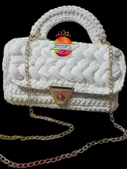 A studio shot of the white t-shirt yarn handbag against a black background. This view clearly shows the top handle and the detachable chain strap.