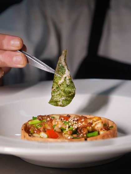 The final garnish of a crispy fried curry leaf is placed on our seasonal vegetable tart, adding an aromatic and textural finishing touch.