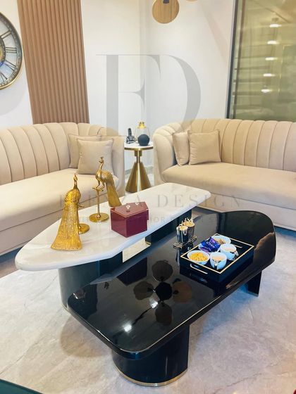 A stylish living room featuring two channel-tufted sofas in a neutral beige, paired with a modern two-tiered coffee table. The black and white marble tops of the table create a striking contrast.