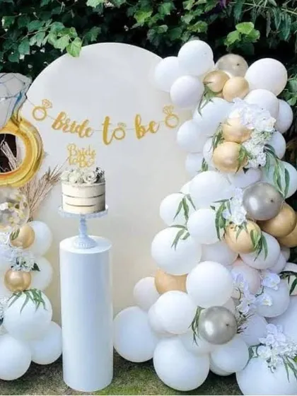 An elegant outdoor 'Bride to be' setup with a white and gold balloon arch, a custom backdrop, and a large diamond ring foil balloon.