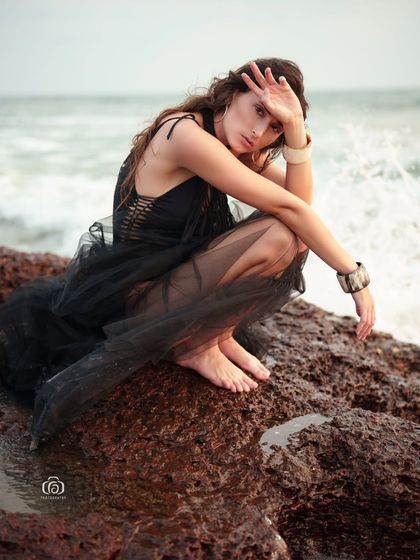 A candid and emotional moment captured on the rocky shore. The model's pose and the crashing waves create a powerful and atmospheric image.