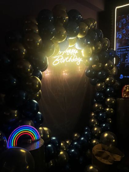 This birthday setup features a full circular balloon arch in blue and silver, with a rainbow neon light prop adding a fun pop of color.
