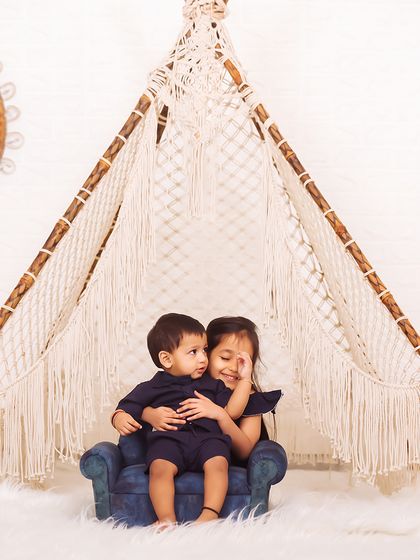 The beginning of a lifelong bond. This sibling portrait captures a sweet, protective hug between an older sister and her baby brother inside a beautiful macrame teepee.
