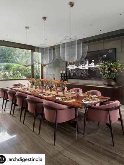 The formal dining room of the K Residence, featuring a long table set for an elegant gathering. The room is illuminated by delicate mesh pendant lights, with a large window offering views of the garden.