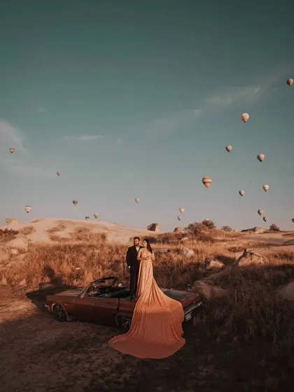The long trail of the peach gown drapes beautifully over the vintage car, creating a romantic and cinematic feel for this destination pre-wedding shoot.