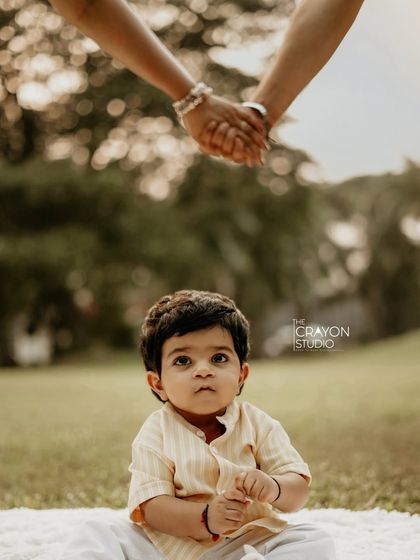 A child sits peacefully, looking up towards the comforting presence of his parents holding hands above him. This artistic shot symbolizes the foundation of love and security that surrounds him.