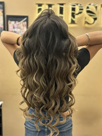 The back view of a client's long, curly hair with a beautiful balayage. The color and curls create a look full of volume and life.