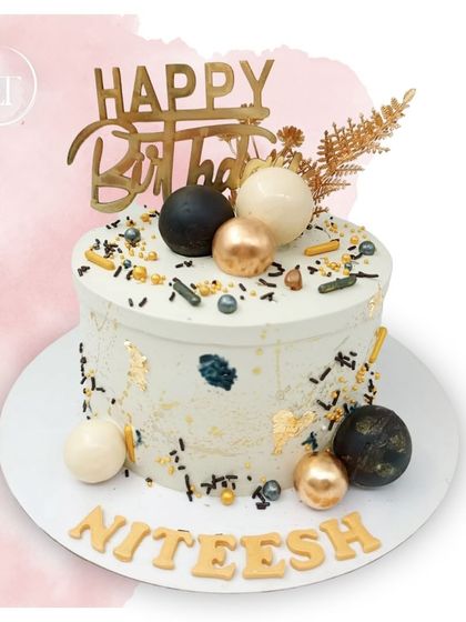 A modern and stylish birthday cake for Niteesh, featuring a black and gold splatter effect and coordinating spheres.