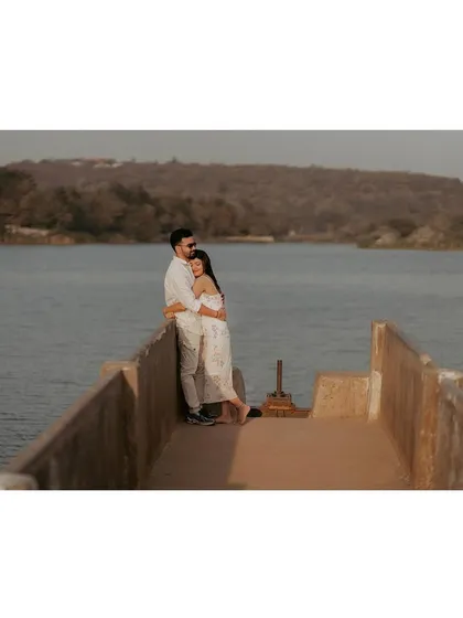 A couple embraces at the end of a pier, looking out over the water together in a peaceful, shared moment.