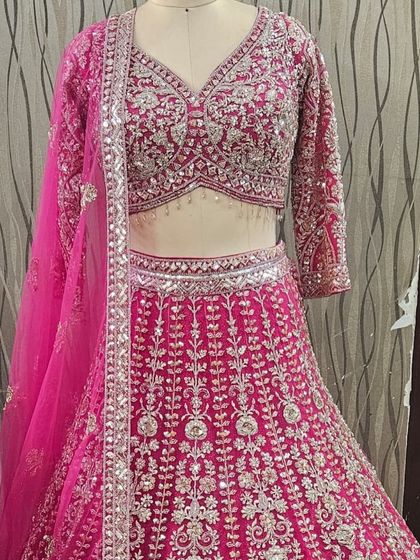 This stunning rani pink lehenga is crafted with intricate silver embroidery and mirror work. It's a vibrant and celebratory choice for any wedding function.