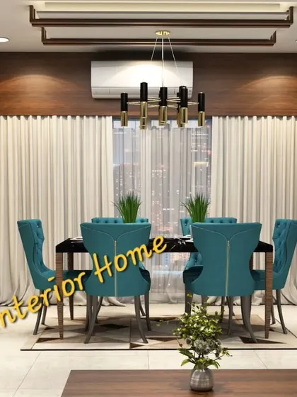 This elegant dining room features plush teal chairs and a modern chandelier. The wooden panel behind the air conditioner cleverly conceals it while adding to the decor.